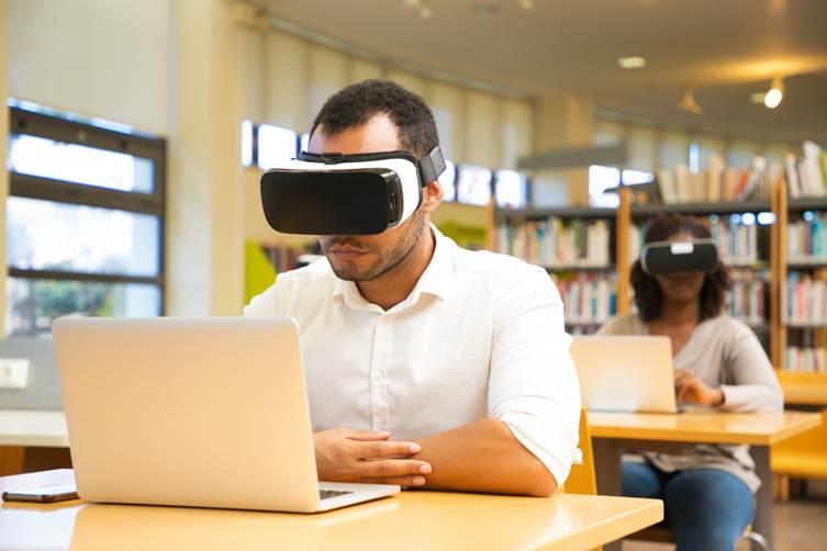 Student using virtual reality headset for AI-powered learning while studying on a laptop in a modern library classroom.