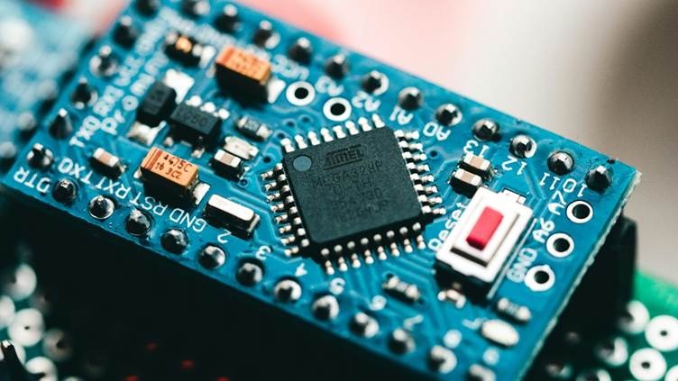 Close-up of a blue Arduino Nano microcontroller board showing the Atmel chip, electronic components, and a small red reset button mounted on the PCB.