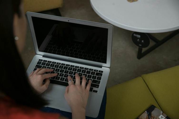 Overhead view of a person typing on a laptop placed on their lap while sitting on a sofa, with a small round table nearby in a casual indoor workspace.
