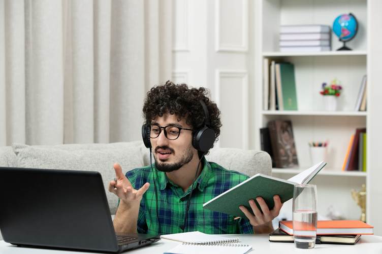 Online learning setup showing a student multitasking with laptop, notebook, and study materials at home