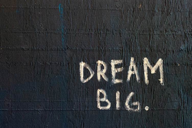 The words “Dream Big.” written in white chalk on a dark wooden surface.