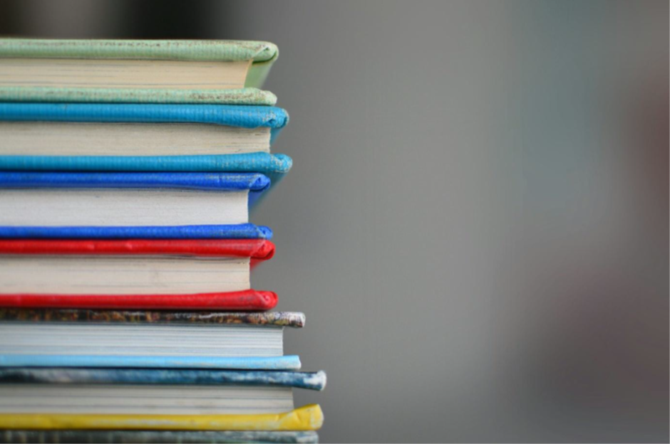 A stack of colorful hardcover books arranged vertically against a blurred background, symbolizing education, learning, and academic preparation.