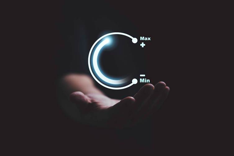 “Hand holding a glowing circular control dial showing minimum to maximum levels, symbolizing adjustment, optimization, or performance control in technology.”
